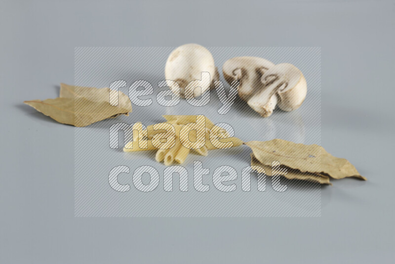 Raw pasta with different ingredients such as cherry tomatoes, garlic, onions, red chilis, black pepper, white pepper, bay laurel leaves, rosemary, cardamom and mushrooms on light blue background