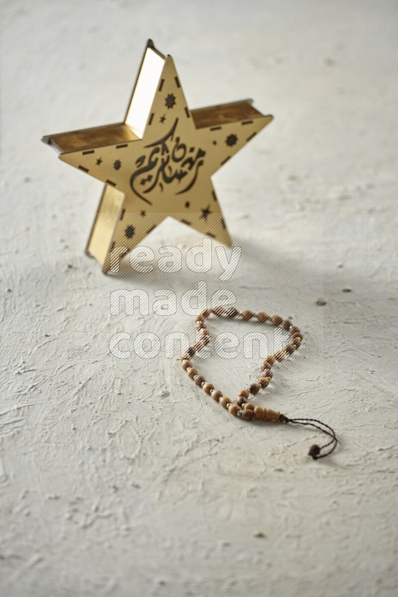 A wooden golden star lantern with different drinks, dates, nuts, prayer beads and quran on textured white background
