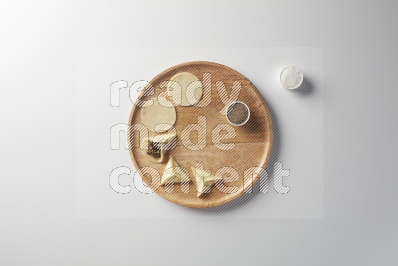 two closed sambosas and one open sambosa filled with meat while salt and black pepper aside in a wooden dish on a white background