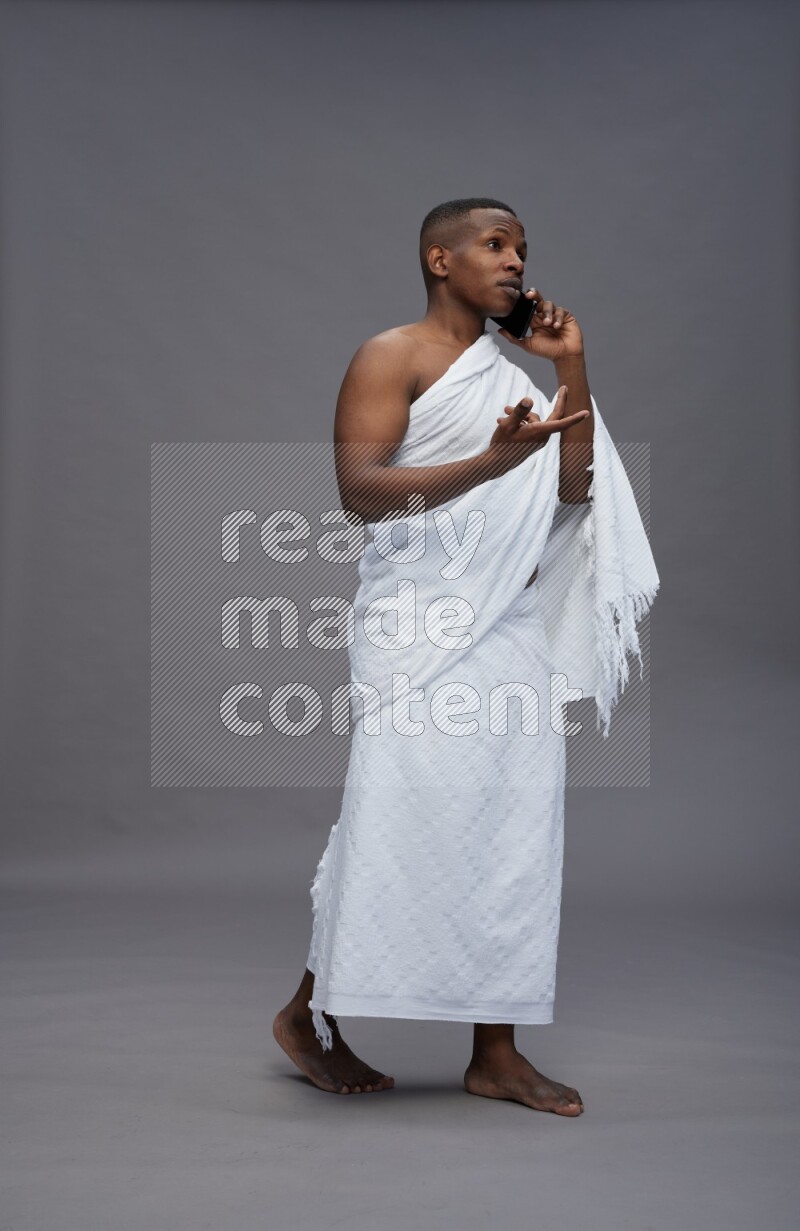 A man wearing Ehram Standing talking on phone on gray background