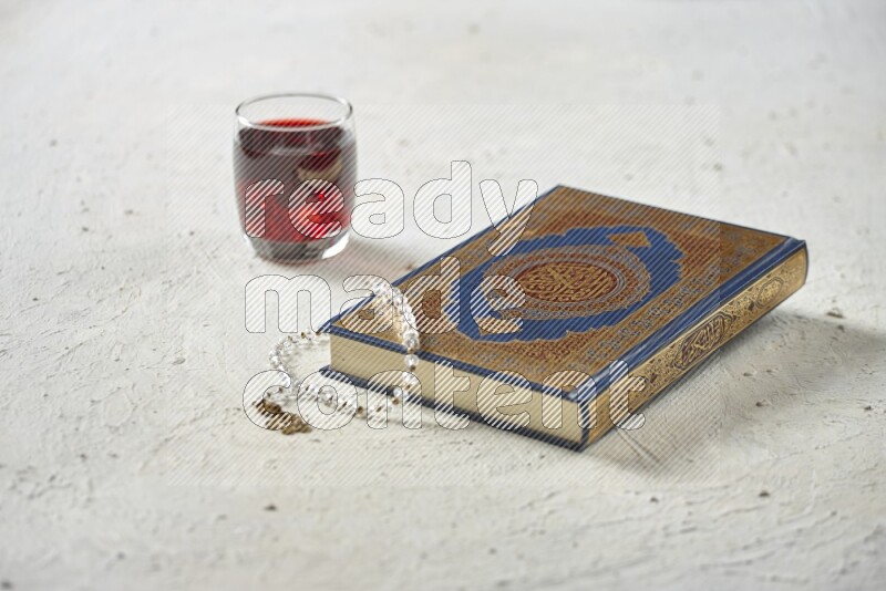 Quran with dates, prayer beads and different drinks all placed on textured white background