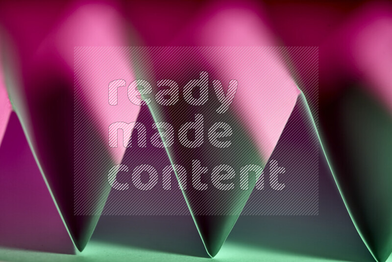 A close-up abstract image showing sharp geometric paper folds in green and pink gradients