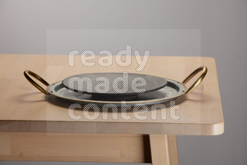 black plate placed on a rounded stainless steel metal tray with golden handels on the edge of wooden table