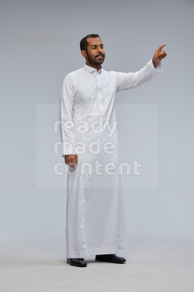 Saudi man Wearing Thob standing interacting with the camera on Gray background