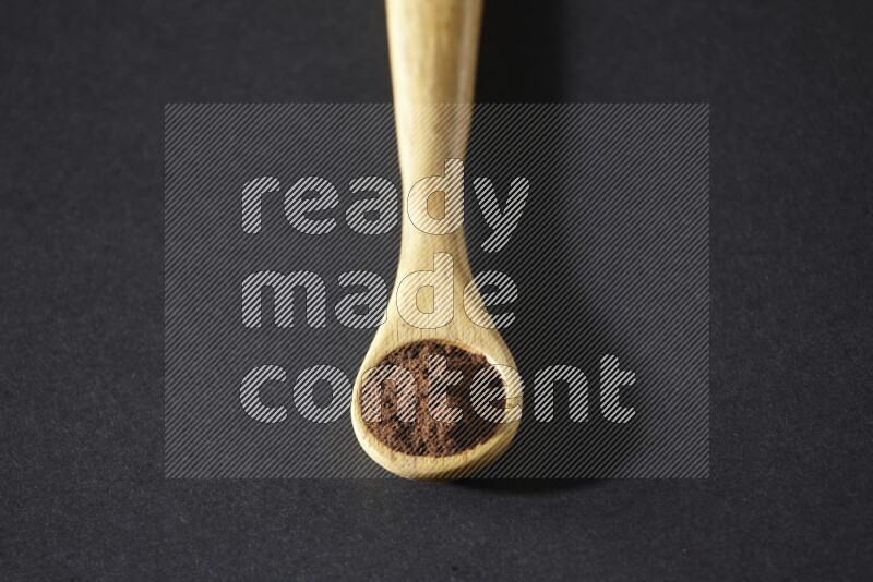 A wooden spoon full of cloves powder on a black flooring