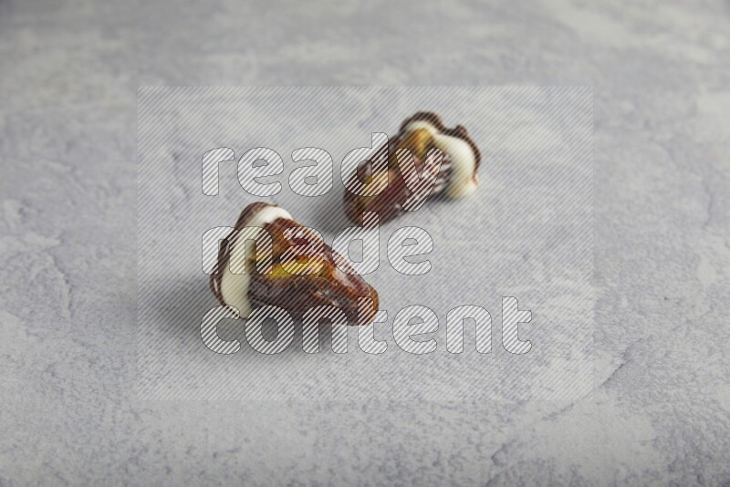 two pistachio stuffed dates covered with white chocolate with dark chocolate drizzle on a light grey background
