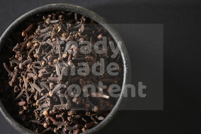 A black pottery bowl full of cloves on a black flooring
