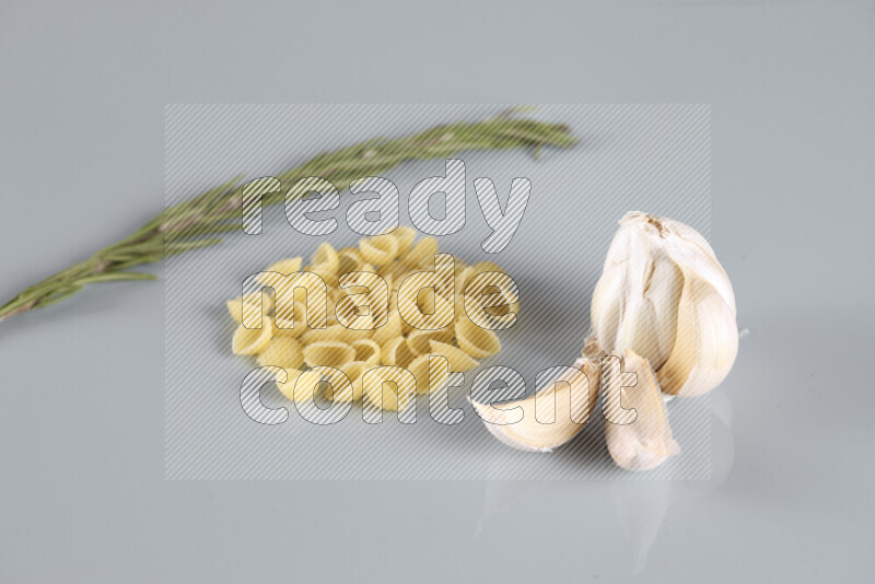 Raw pasta with different ingredients such as cherry tomatoes, garlic, onions, red chilis, black pepper, white pepper, bay laurel leaves, rosemary, cardamom and mushrooms on light blue background
