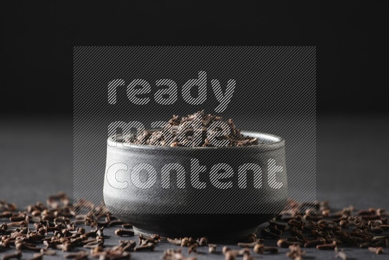 وعاء فخاري أسود ممتلئ بحبوب القرنفل علي خلفية سوداء