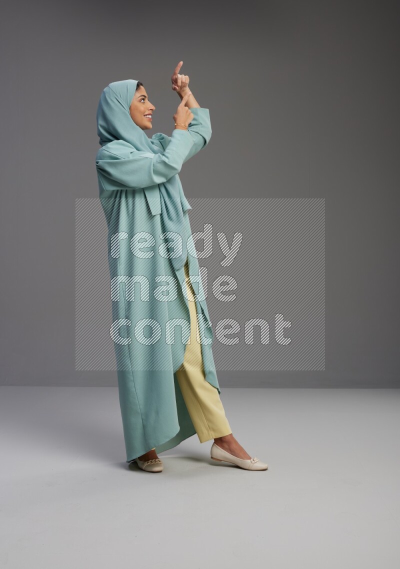 Saudi Woman wearing Abaya standing interacting with the camera on Gray background