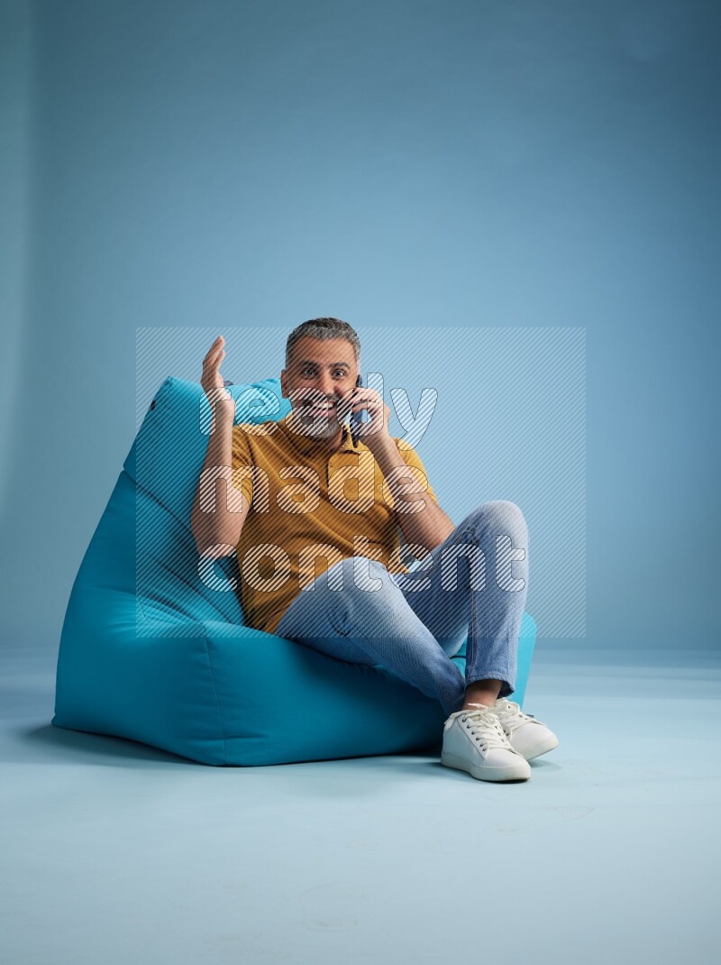 A man sitting on a blue beanbag and talking on the phone