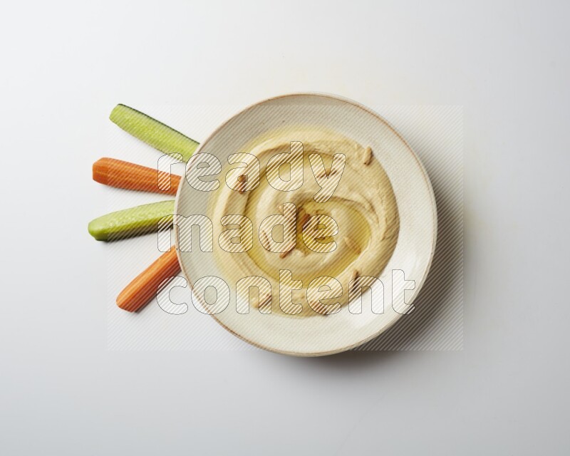 Hummus in a pottry plate garnished with pine nuts on a white background
