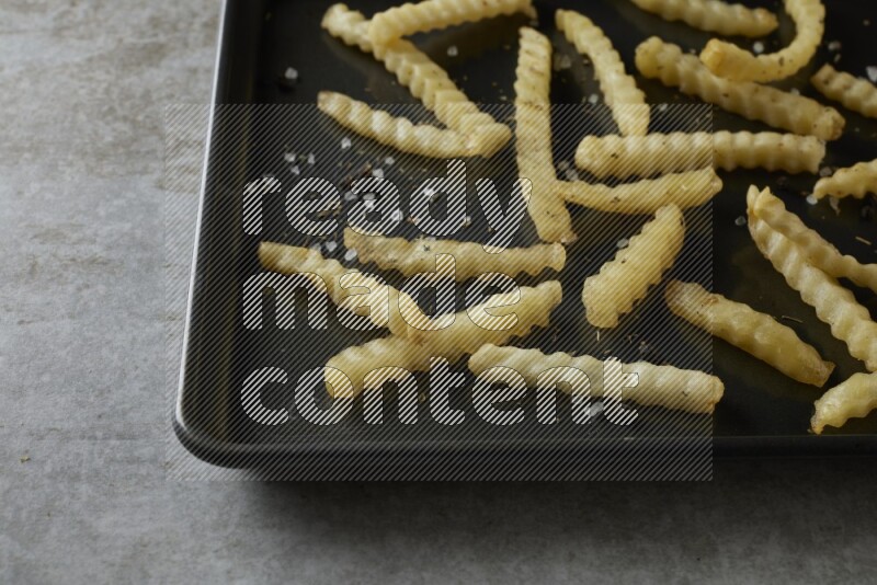 crinkle fries in a black stainless steel rectangle tray on grey textured counter top