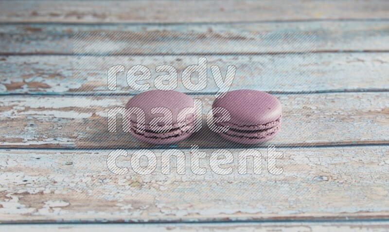 45º Shot of two Purple Blueberry macarons on light blue wooden background