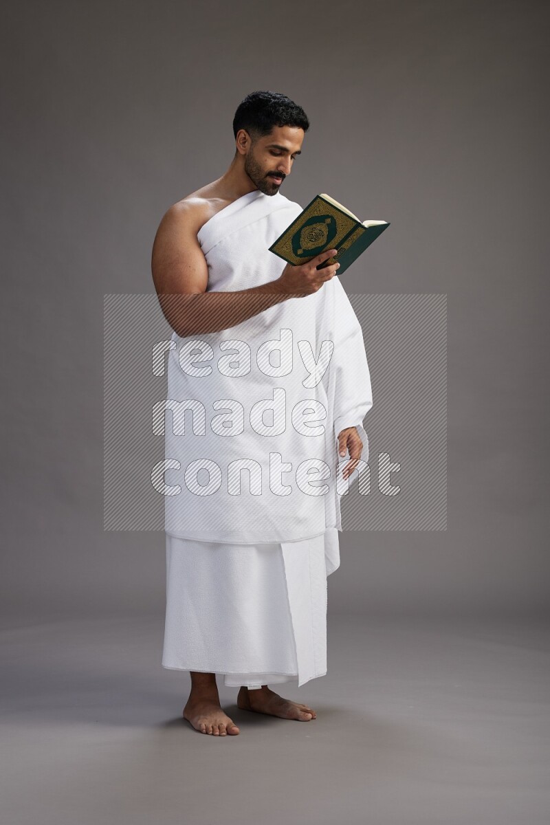 A man wearing Ehram Standing reading quran on gray background