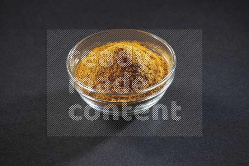 A glass bowl full of turmeric powder on black flooring