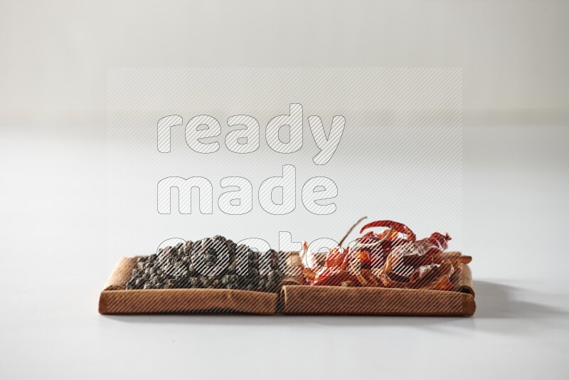 مربعان من أعواد القرفة ممتلئان بالفلفل الحار المجفف وحبوب الفلفل الأسود علي خلفية بيضاء