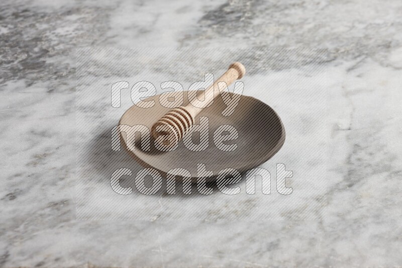 Multicolored pottery plate with wooden honey dipper in it on grey marble background