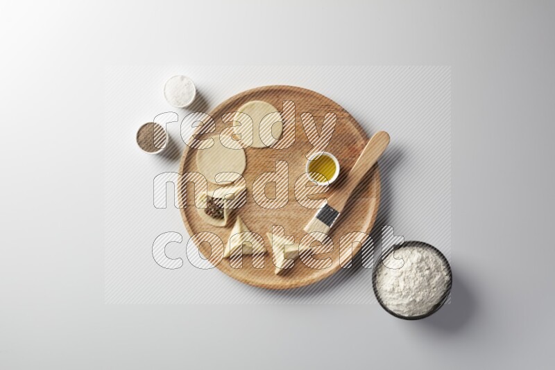 two closed sambosas and one open sambosa filled with meat while flour, salt, black pepper and oil with oil brush aside in a wooden dish on a white background