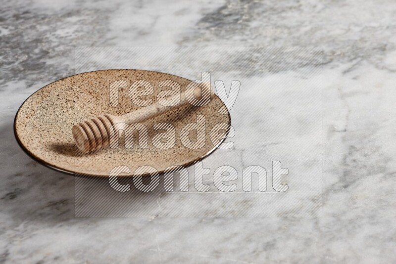 Multicolored pottery plate with wooden honey dipper in it on grey marble background