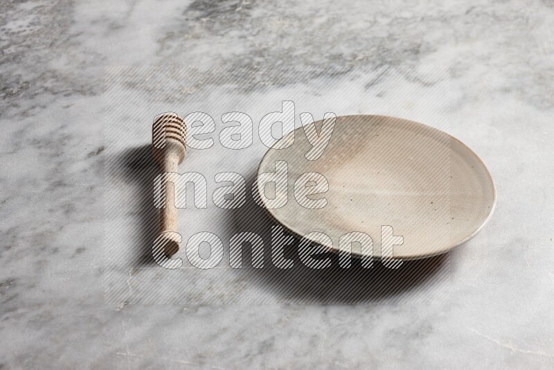 Multicolored pottery plate with wooden honey dipper on the side on grey marble background