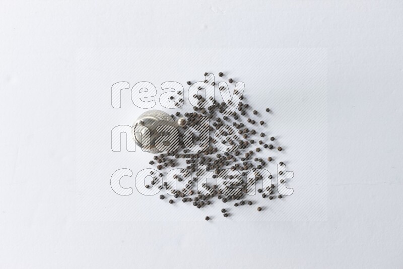 مطحنة فلفل تركية معدنية وحبوب فلفل أسود متناثرة على أرضية بيضاء