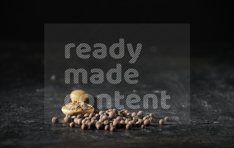 ملعقة خشبية ممتلئة ببودرة بهار الفلفل الحلو بجانب حبوب من الفلفل على خلفية سوداء