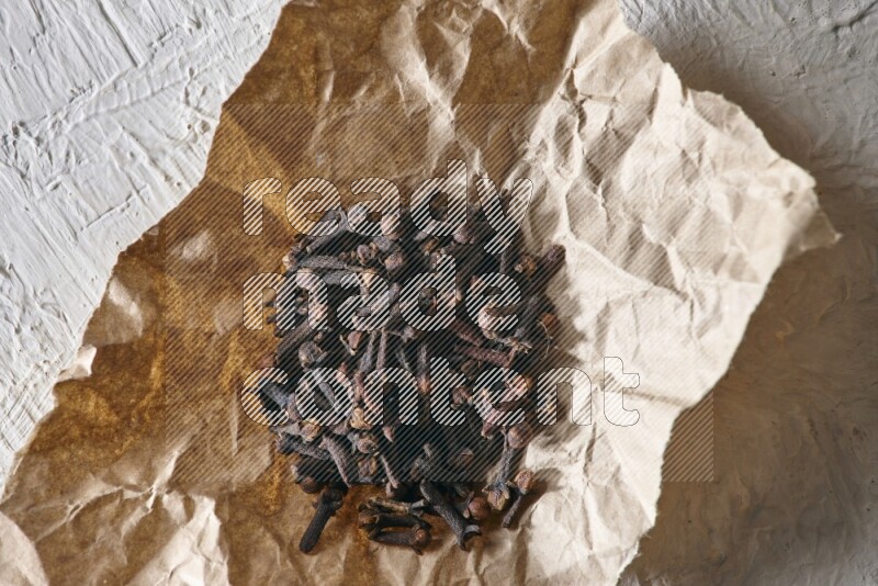 Cloves on crumpled piece of paper on a textured white flooring
