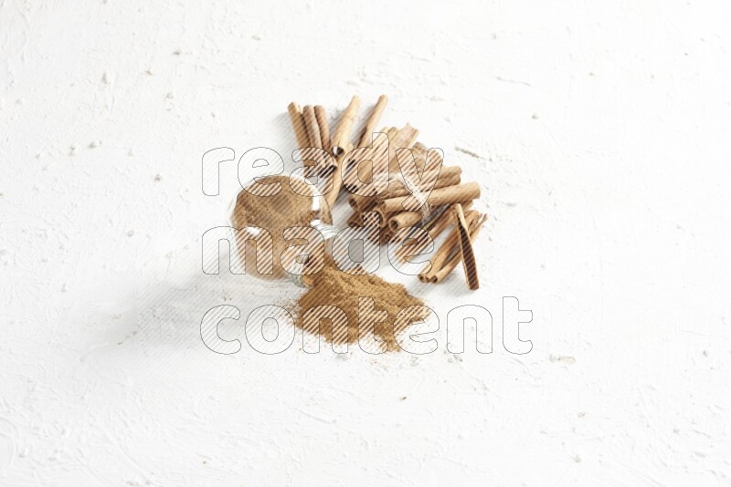 Flipped herbs glass jar full of cinnamon powder and cinnamon sticks in the back on a textured white background