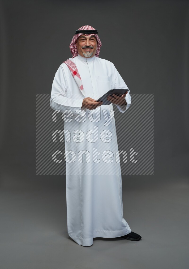 Saudi man with shomag Standing working on tablet on gray background
