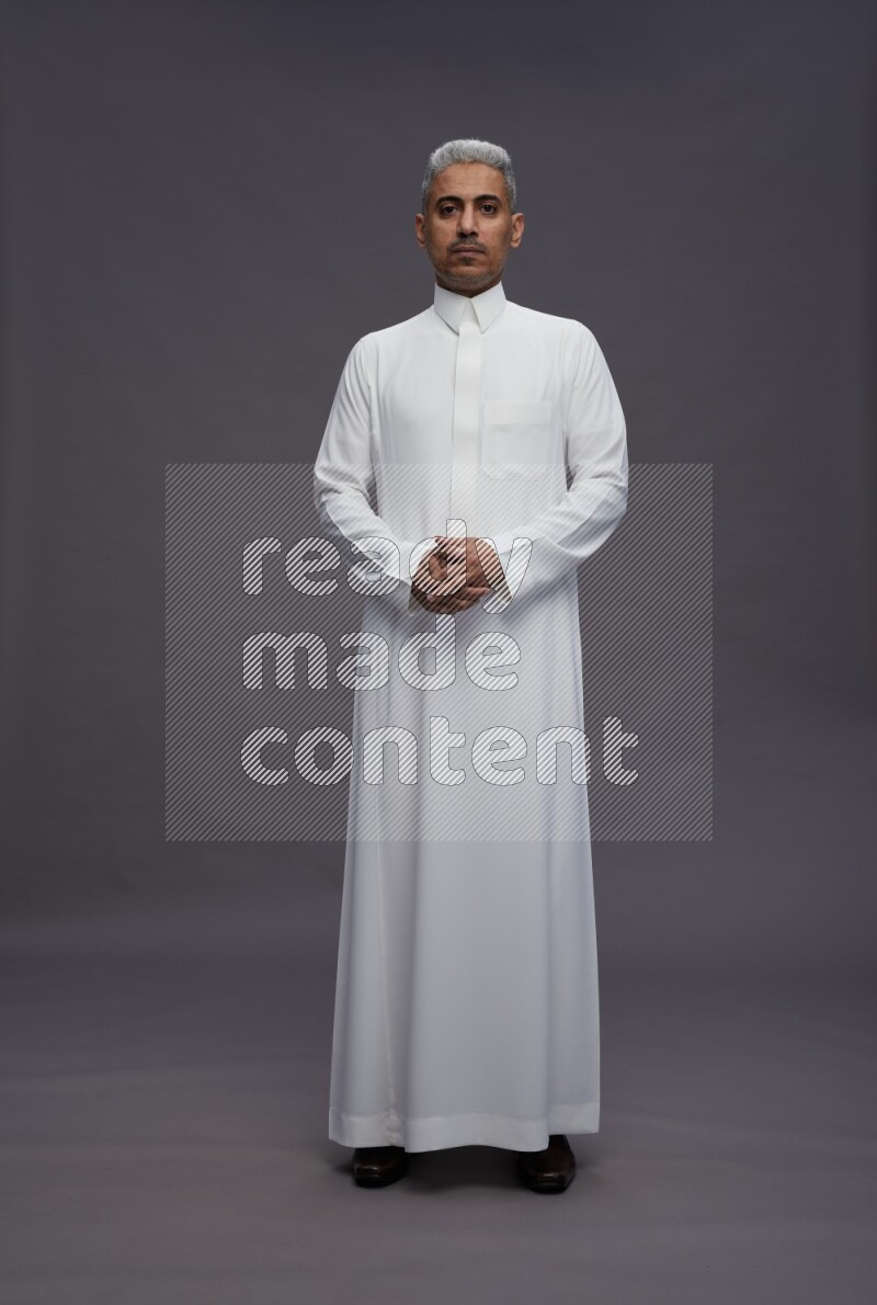Saudi man wearing thob standing interacting with the camera on gray background