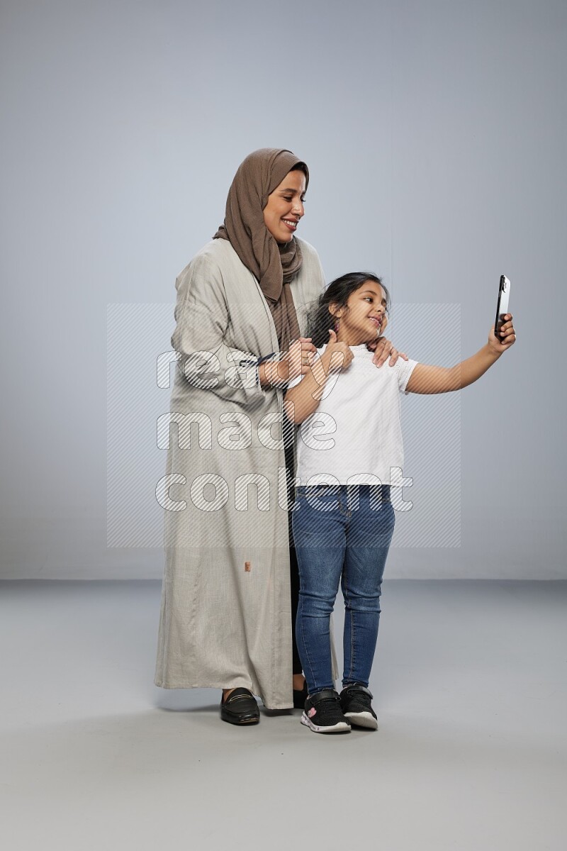 A girl standing taking selfie with her mother on gray background