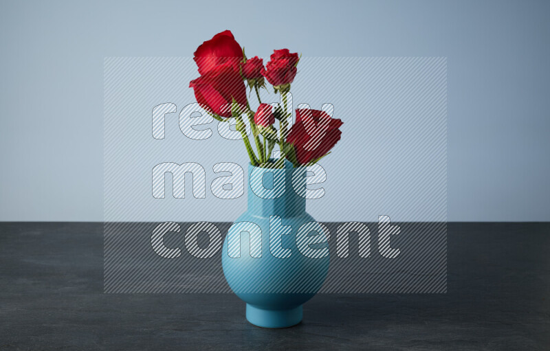 An arrangement of vivid red roses in a blue vase on black marble background