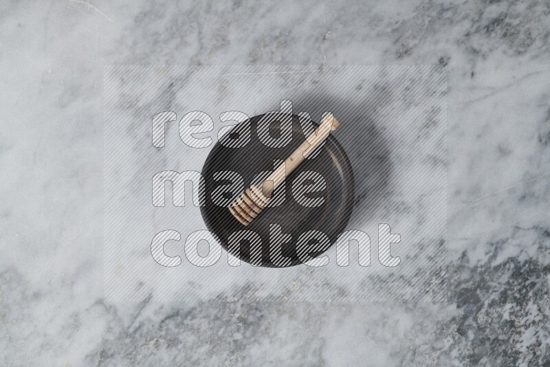 Black pottery oven plate with wooden honey dipper in it on grey marble background