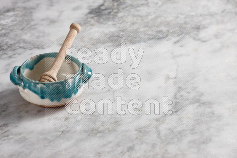 Multicolored pottery bowl with wooden honey dipper in it on grey marble background