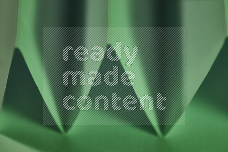 A close-up abstract image showing sharp geometric paper folds in green gradients