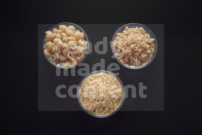 Different pasta types in glass bowls on black background