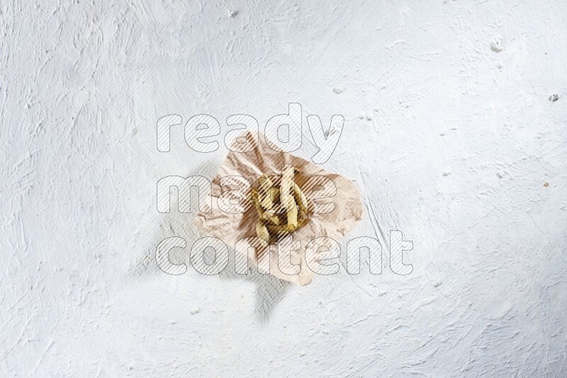 Dried turmeric whole fingers in a crumpled piece of paper on textured white flooring