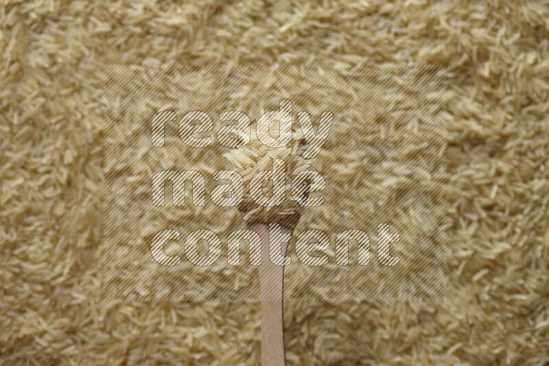 A wooden spoon full of basmati golden rice on basmati golden rice background