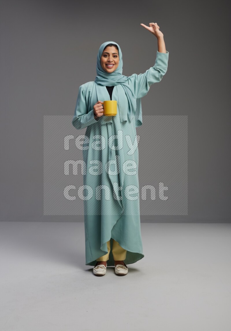 Saudi Woman wearing Abaya standing  holding a mug on Gray background