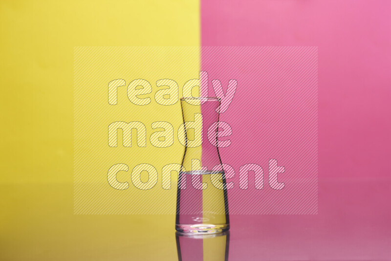 The image features a clear glassware filled with water, set against yellow and pink background