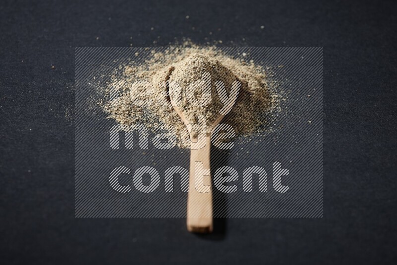 A wooden spoon full of cardamom powder and powder spreaded on black flooring