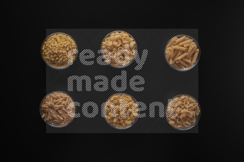 Different pasta types in 6 glass bowls on black background