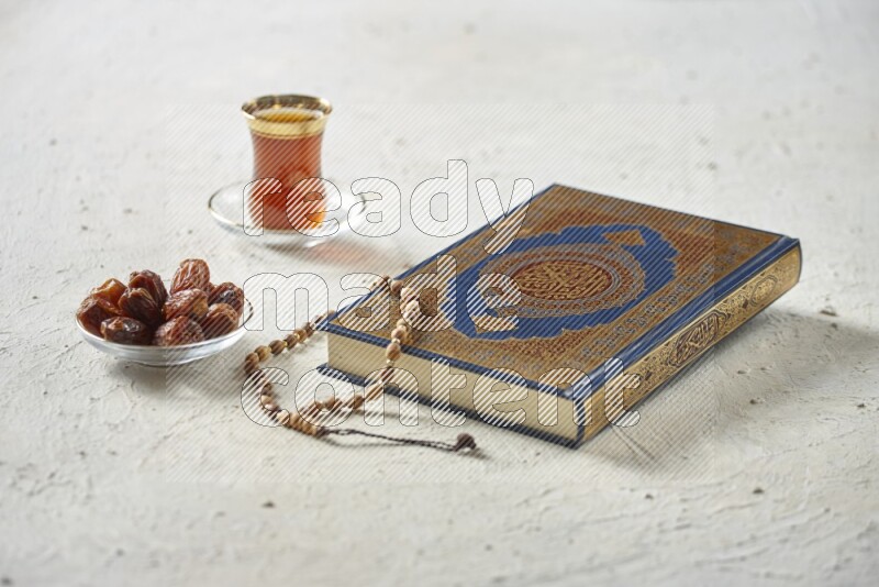 Quran with dates, prayer beads and different drinks all placed on textured white background