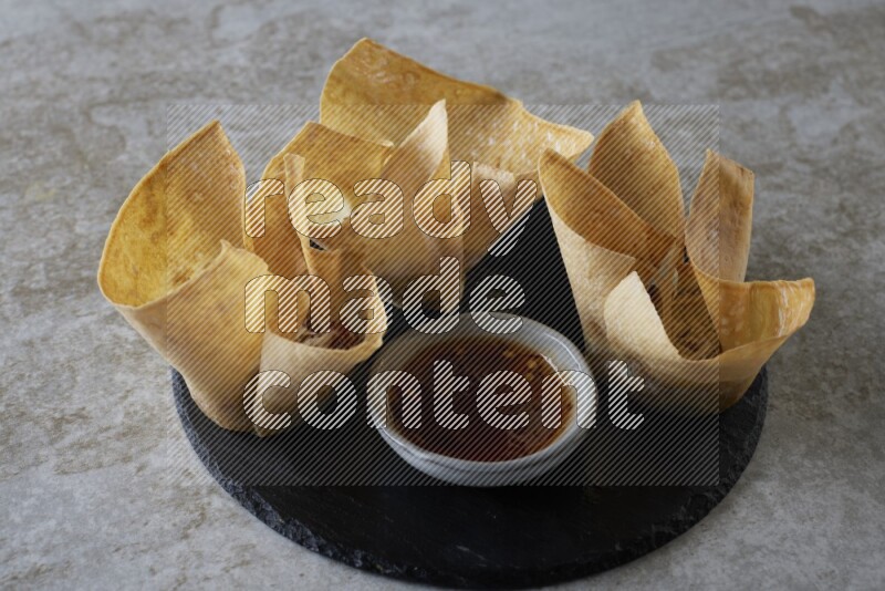 wonton cups with soy sauce ramkin on circle slate on grey textured counter top