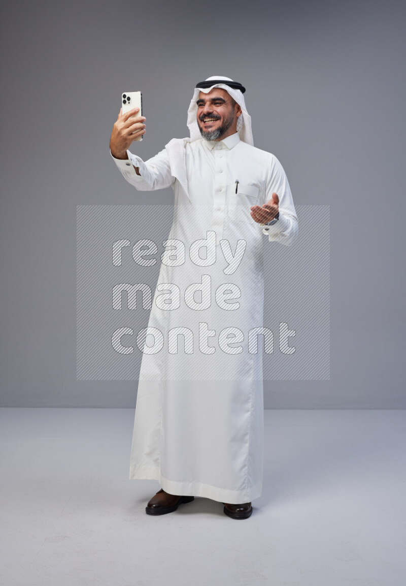 Saudi man Wearing Thob and white Shomag standing taking selfie on Gray background