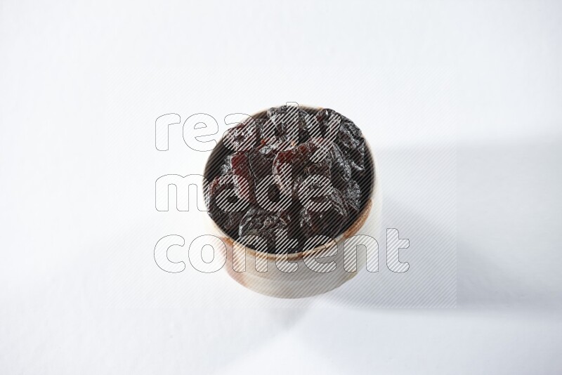 A beige ceramic bowl full of dried plums on a white background in different angles