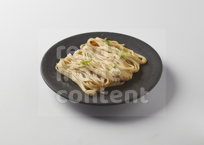 spaghetti pasta with white sauce on a black plate on a white background