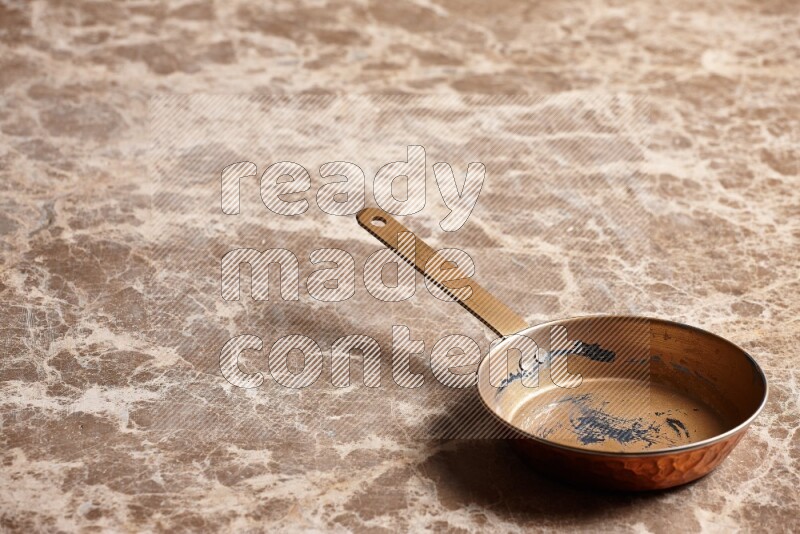 A small copper pan on beige marble background