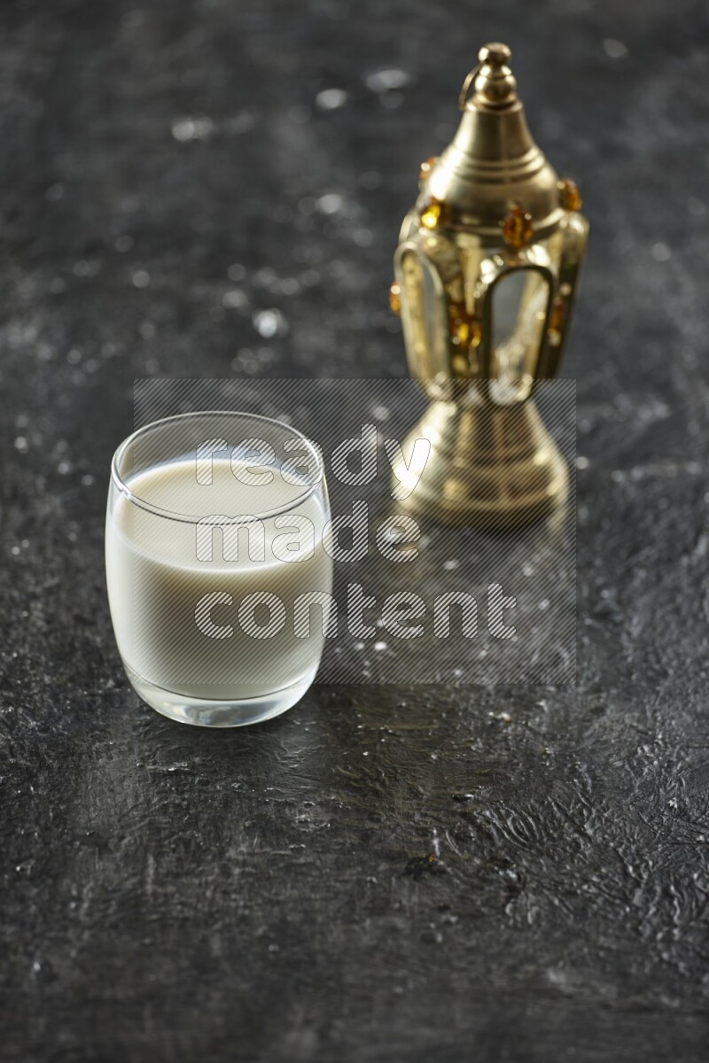A golden lantern with different drinks, dates, nuts, prayer beads and quran on textured black background
